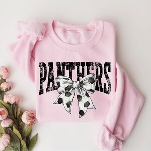 A pink sweatshirt with the word "PANTHERS" and a soccer ball bow printed on it, along with some pink flowers.