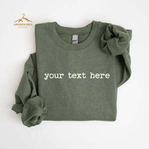 May include: A green crew neck sweatshirt with the text "your text here" printed in white on the front.