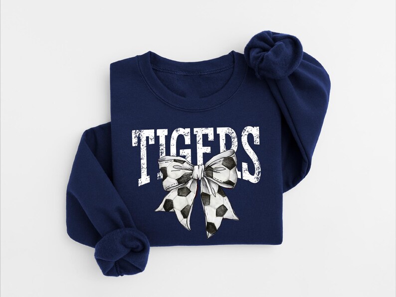 A navy blue sweatshirt with the word "TIGERS" printed on it, along with a large white bow featuring soccer balls.