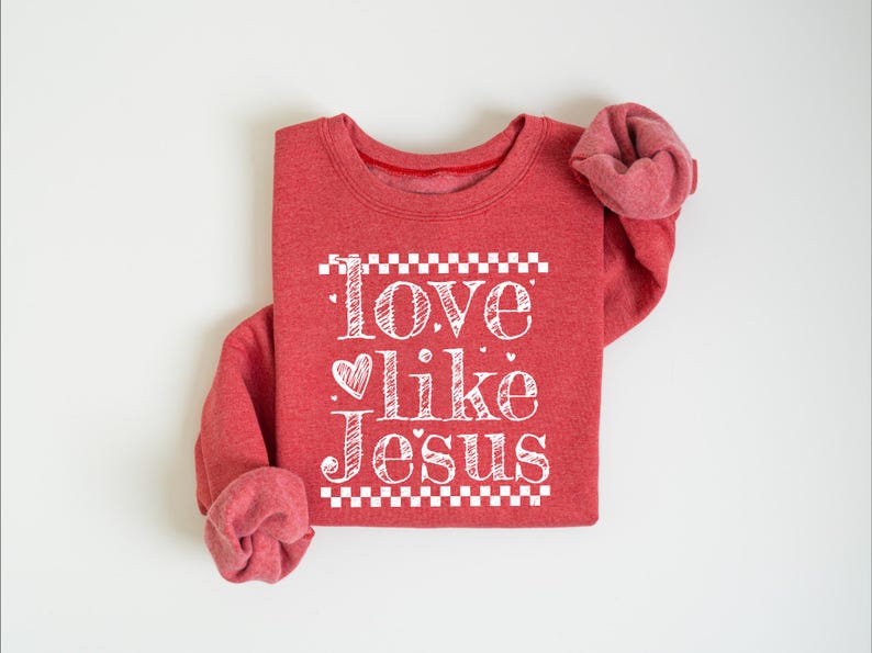 Puede incluir: Sudadera roja con la frase "Love like Jesus" en letras blancas. El texto est&aacute; centrado en la parte delantera de la prenda, con un coraz&oacute;n en lugar de la palabra "love". La sudadera tiene mangas largas y cuello redondo.