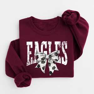 A burgundy sweatshirt with the word "EAGLES" printed on it, along with a bow design.