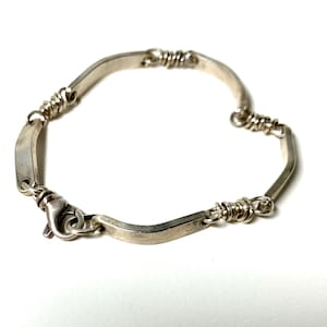 May include: A silver bracelet with a unique design featuring flat, rectangular links connected by twisted wire accents. The bracelet has a secure clasp.