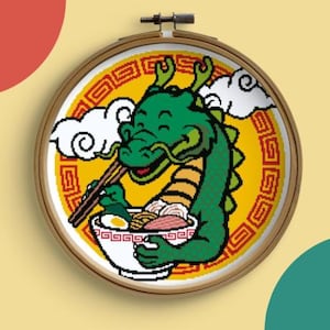 Puede incluir: Un bastidor de bordado de punto de cruz con un dragón verde disfrutando de un cuenco de ramen. El dragón sostiene palillos y un cuenco con fideos, huevo y carne. El fondo es amarillo con un patrón rojo y blanco, y nubes blancas.