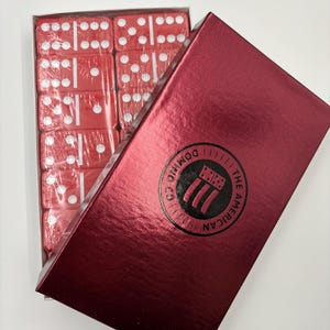 May include: A set of red dominoes in a red box with the text "The American Domino Co." printed on the box.