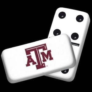 May include: A set of white dominoes with black dots. One domino has the Texas A&M logo in maroon.