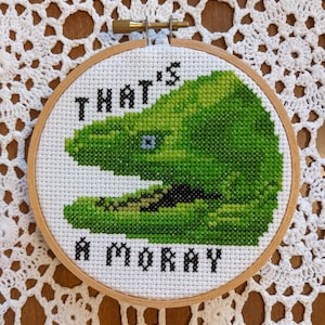 May include: A white embroidery hoop with a green and black embroidered image of a creature with the text "That's a Moray" underneath.
