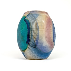 May include: A ceramic vase with a rounded body and a narrow opening, featuring a multi-colored glaze in shades of turquoise, deep blue, soft pink, and cream. The surface displays textured horizontal grooves and abstract, layered color washes.