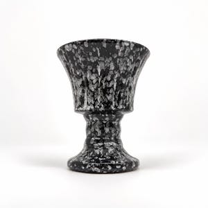 May include: A black and white speckled goblet with a wide, flared rim and a sturdy, thick stem. The surface features a mottled, high-contrast pattern of irregular white spots against a deep black base, creating a textured appearance throughout.