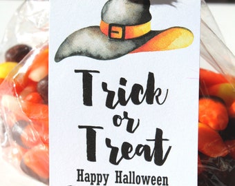 May include: A clear cellophane bag filled with candy corn and other candies. A white tag with a watercolor witch hat illustration and the words "Trick or Treat" and "Happy Halloween From The Emersons" is attached with yellow and white twine.