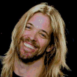 May include: A man with long blonde hair smiles broadly at the camera. He is wearing a black shirt.