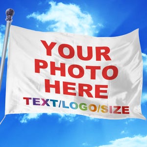 以下が含まれることがあります： 赤い文字で「YOUR PHOTO HERE TEXT/LOGO/SIZE」と書かれた白い旗。旗は青い空と白い雲を背景に風になびいている。