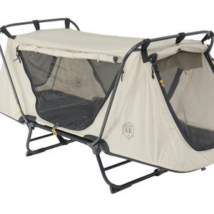May include: A beige camping cot with a tent-like structure. The cot has a black metal frame and a mesh window. The tent has a beige fabric exterior and a black mesh window. The cot is designed for outdoor use.