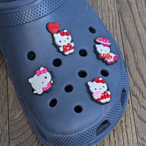 Könnte beinhalten: Blauer Schuh mit vier Hello Kitty-Anhängern. Die Anhänger sind rot, pink und weiß. Ein Anhänger hat ein rotes Herz mit dem Wort "Love" darauf.