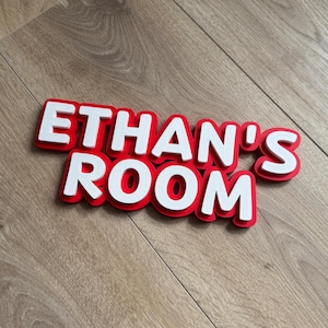 Könnte beinhalten: Rote und weiße 3D-Buchstaben, die "Ethan's Room" auf einem Holzgrund bilden.