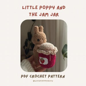 Peut inclure: Un lapin crocheté tenant un pot de confiture crocheté avec un motif de fraise. Le texte "LITTLE POPPY AND THE JAM JAR" et "PDF CROCHET PATTERN" sont affichés au-dessus et en dessous de l'image.
