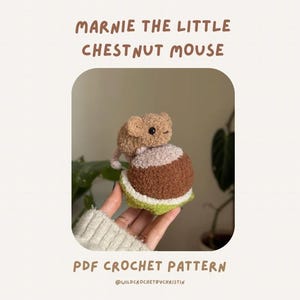 Puede incluir: Un juguete de peluche de ganchillo de un ratón pequeño de color canela sentado sobre una castaña marrón y blanca con una base verde. El texto dice MARNIE THE LITTLE CHESTNUT MOUSE y PDF CROCHET PATTERN. El ratón tiene ojos negros.
