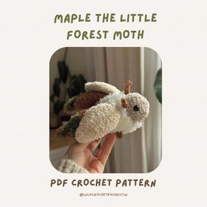 Op de afbeelding: Een gehaakt mot-speelgoed met crèmekleurige vleugels, bruine antennes en een bruin lichaam. De tekst "MAPLE THE LITTLE FOREST MOTH" en "PDF CROCHET PATTERN" staan boven en onder de mot.
