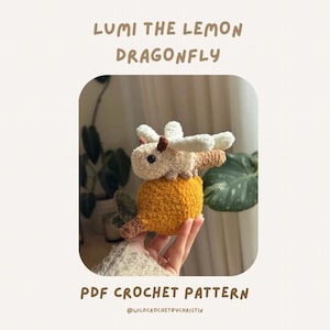 May include: A handmade crochet lemon dragonfly toy. The toy is yellow with a white head and wings, and brown accents. The text "LUMI THE LEMON DRAGONFLY" and "PDF CROCHET PATTERN" are displayed on the image.