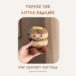 May include: A crocheted pancake-shaped toy in shades of brown, tan, and yellow, with a smiling face. The text "TOFFEE THE LITTLE PANCAKE" is above the toy, and "PDF CROCHET PATTERN" is below. The toy has two small brown ball-shaped feet.