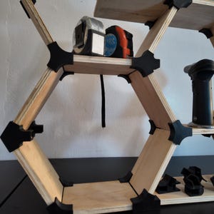 Könnte beinhalten: Ein sechseckiges Holzregal mit Werkzeugen. Das Regal hat eine helle Holzoberfläche mit schwarzen Verbindern. Werkzeuge wie Maßbänder und ein schwarzer Brenner sind zu sehen. Modernes Design.