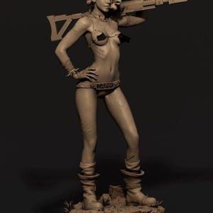 May include: A clay sculpture of a woman with a mohawk hairstyle, wearing a bikini top and bottoms, holding a rifle over her shoulder. She has tattoos on her arms and legs, and is wearing boots. The sculpture is on a base with grass and a box.