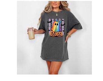 Könnte beinhalten: Dunkelgraues T-Shirt mit einem bunten Geistermotiv. Der Geist ist regenbogenfarben und trägt eine blaue Schleife, die auf zwei orangefarbenen Kürbissen sitzt. Das Shirt hat eine lockere Passform und ist für Halloween geeignet.