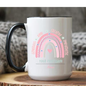 Puede incluir: Taza de cerámica blanca con asa y borde negros. La taza presenta un diseño de arcoíris rosa con las palabras "Generoso, Amable, Creativo, Empático" y el texto "TU PROFESIÓN" y un nombre.
