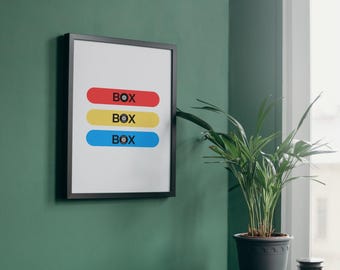 Puede incluir: Una impresión enmarcada con la palabra "BOX" repetida tres veces en texto negro sobre formas rectangulares de colores. Las formas son roja, amarilla y azul. La impresión está colgada en una pared verde.