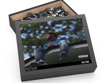 Puede incluir: Una caja de rompecabezas negra con la imagen de una persona sentada en un tejado, con el texto "2014 FOREST HILLS DRIVE". La caja está abierta, revelando piezas de rompecabezas. La caja está etiquetada como "8x10 Puzzle" y "120 piezas Edades 9+".