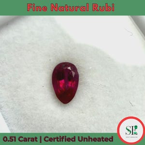 May include: A deep red, pear-shaped ruby gemstone. The gem is displayed against a white background. Text at the top reads "Fine Natural Rubi" and at the bottom "0.51 Carat | Certified Unheated".