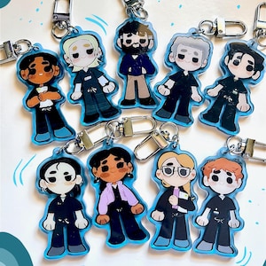 Puede incluir: Una colección de llaveros de personajes de dibujos animados. Cada llavero presenta un diseño de personaje diferente con un contorno azul y un cierre plateado. Los personajes visten varios atuendos, con diversos tonos de piel y peinados.