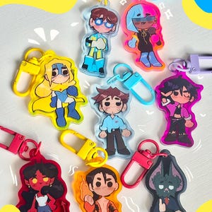 Könnte beinhalten: Eine Sammlung farbenfroher Acryl-Schlüsselanhänger mit Cartoon-Charakteren in verschiedenen Designs. Jeder Schlüsselanhänger hat ein einzigartiges Charakterdesign mit leuchtenden Farben und Metallverschlüssen in Gelb, Rosa und Blau.