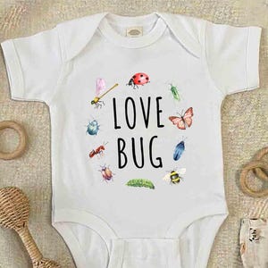 May include: A white ceramic mug with a black handle and the text "But First, Coffee" in a handwritten style. The mug is on a white surface. The mug is approximately 10 cm tall.