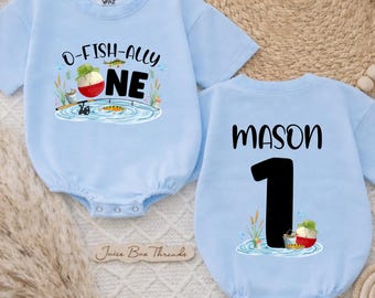 May include: Light blue baby bodysuit with the text "O-FISH-ALLY ONE" and a fishing-themed graphic on the front. The back of the bodysuit has the name "MASON" and the number "1". The bodysuit is short-sleeved.