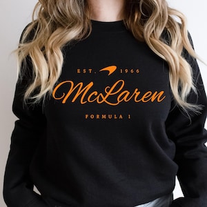 May include: Black sweatshirt with an orange McLaren Formula 1 logo and the text "EST. 1966"