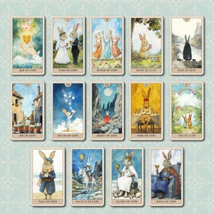 K&ouml;nnte beinhalten: Ein Kartenset mit Tarotkarten, die fantasievolle Illustrationen von Kaninchen in verschiedenen Szenen zeigen. Die Karten sind mit Zahlen und Titeln wie "As der Kelche" und "Zwei der Kelche" beschriftet. Das Wort "Cups" steht oben.