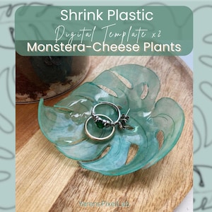 Op de afbeelding: Een turquoise, bladvormige sieradenschaal met twee ringen. De schaal is gemaakt van doorschijnend plastic en staat op een houten oppervlak. De tekst "Shrink Plastic Digital Template x2 Monstera-Cheese Plants" is zichtbaar.