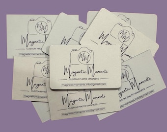May include: A stack of business cards for a company called "Magnetic Moments" that specialises in custom photo magnets. The cards are beige with black text and a simple camera icon.