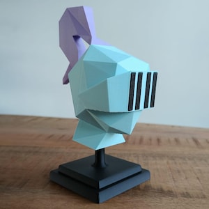 Peut inclure: Une figurine de casque de chevalier géométrique bleu clair et violet sur un socle noir. Le casque a une visière avec des accents noirs.