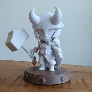 Op de afbeelding: Een wit 3D-geprint beeldje van een personage dat een hamer vasthoudt. Het personage draagt een helm met hoorns en een cape. Het beeldje staat op een bruine basis.