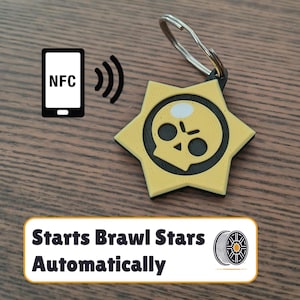 Puede incluir: Un llavero de estrella amarilla con un diseño de calavera negra. El llavero tiene un anillo plateado y se puede usar con NFC para iniciar automáticamente el juego Brawl Stars.