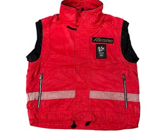 May include: A red and black Mizuno vest with a high collar and a zipper closure. The vest has a reflective stripe across the chest and a small patch with the Mizuno logo and Olympic rings. The vest is a vintage style.