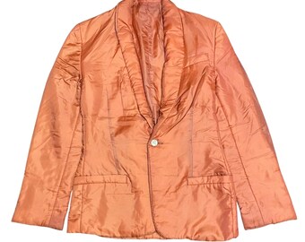 May include: A quilted blazer in a solid copper-orange color featuring a shawl collar, long sleeves, and a single-button front closure. The garment includes two horizontal welt pockets at the waist and a smooth, slightly reflective fabric finish.