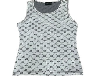 May include: A sleeveless tank top in a light gray color featuring a repeating black Gucci logo pattern across the entire fabric. The garment has a round neckline and a black label at the inner collar with the text GUCCI printed in white.