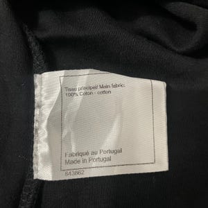 Puede incluir: Primer plano de una prenda negra con una etiqueta blanca. La etiqueta dice "Tissu principal/ Main fabric: 100% Coton - cotton" y "Fabriqu&eacute; au Portugal Made in Portugal". Tambi&eacute;n es visible el n&uacute;mero "843862".
