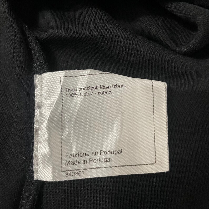 Puede incluir: Primer plano de una prenda negra con una etiqueta blanca. La etiqueta dice "Tissu principal/ Main fabric: 100% Coton - cotton" y "Fabriqu&eacute; au Portugal Made in Portugal". Tambi&eacute;n es visible el n&uacute;mero "843862".