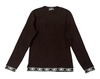 May include: A long-sleeved brown shirt with a crew neck. The cuffs and hem feature a repeating pattern of a logo in black and white. The shirt has a small tag at the neckline with the brand name.