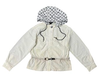 May include: White jacket with a hood featuring a black and white pattern. The jacket has a drawstring hood, a cinched waist with a belt, and a button closure. The jacket's sleeves are long and the overall style is casual.