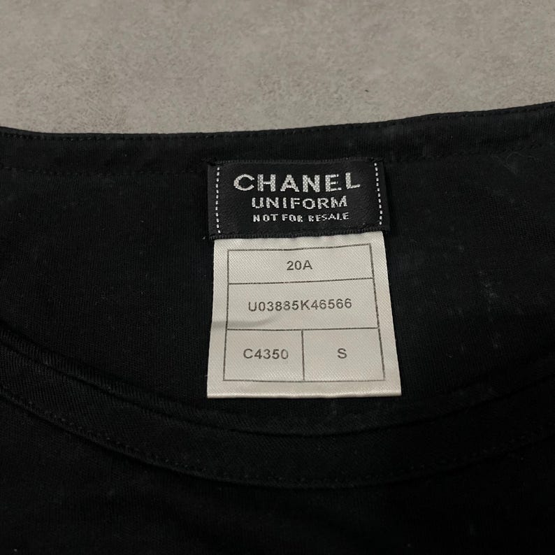 Puede incluir: Primer plano de una prenda negra con una etiqueta que dice "CHANEL UNIFORM NOT FOR RESALE". La etiqueta tambi&eacute;n incluye los n&uacute;meros "20A", "U03835K46566", "C4350" y la letra "S".