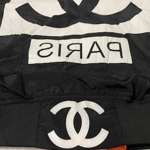 May include: Black and white jacket with the word "PARIS" in white block letters. The jacket features a large white logo on the top and bottom. The jacket is made of a shiny material.